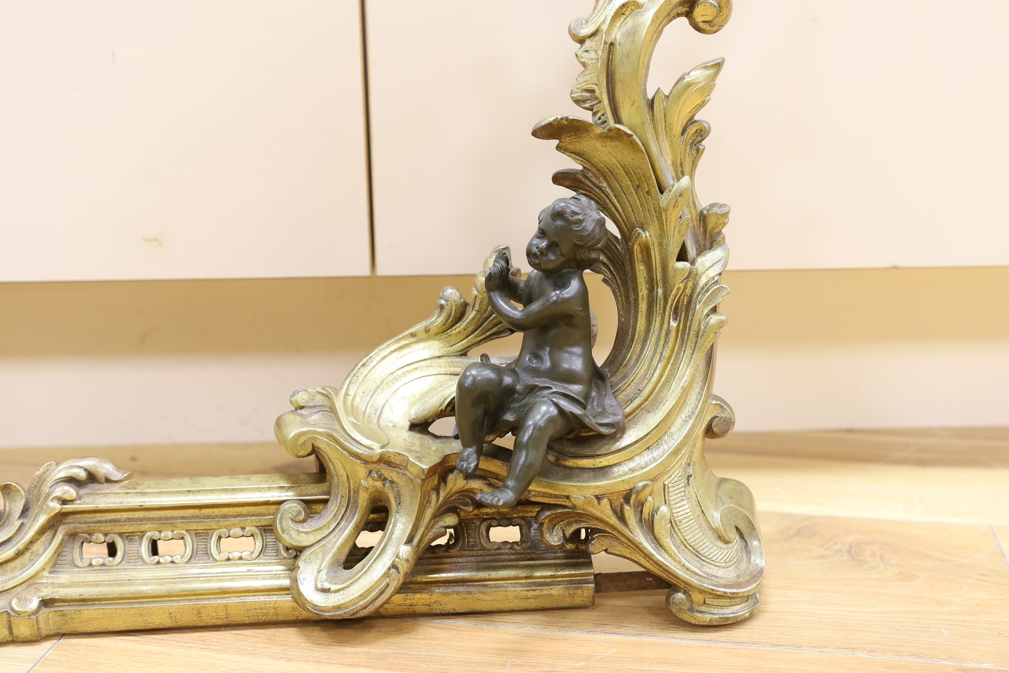 A pair of brass chenet mounted with patinated bronze figures of putti, 97cm wide